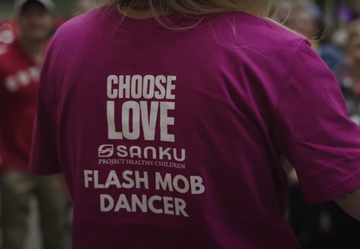 Woman with magenta t-shirt that says Choose Love Sanku Project Healthy Children Flash Mob Dancer on the back in white lettering